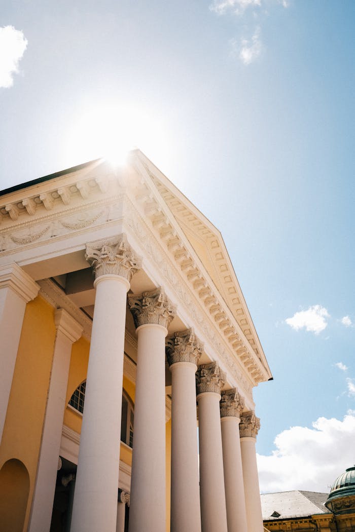 about-us A stunning view of classical architectural columns under a bright blue sky, showcasing elegance and heritage.